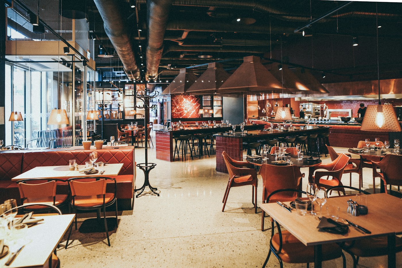 Salão amplo de restaurante com mesas e cozinha aberta ao fundo